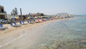 A beach with clear shallow waters, rows of blue lounge chairs, and colorful umbrellas. - Haris Apartments (Hersonissos)