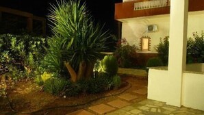 A building with a white facade, a balcony, and a garden with a large tree and shrubs. - Haris Apartments (Hersonissos)