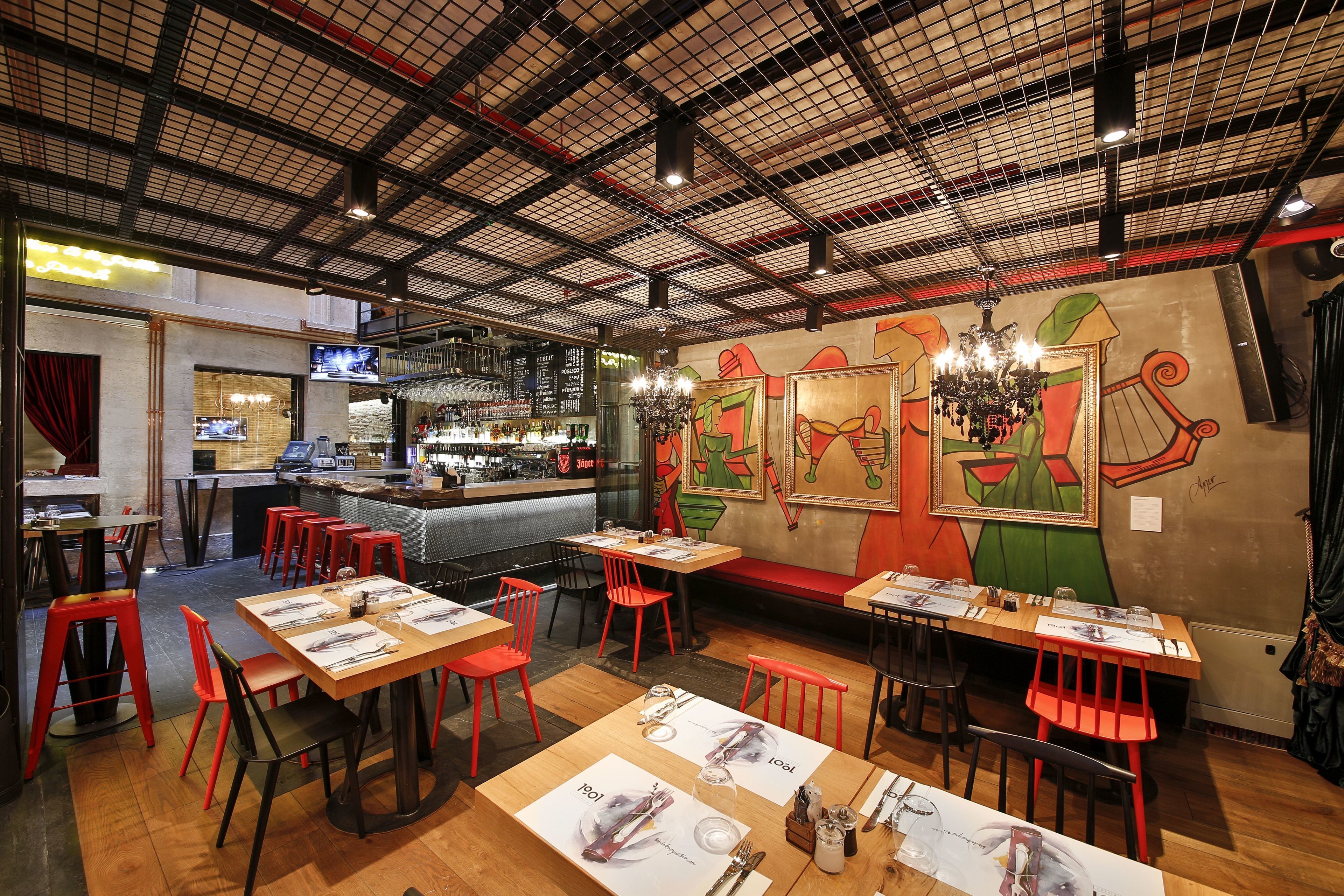 Un restaurant avec de hauts plafonds, des chaises rouges et un coin bar.