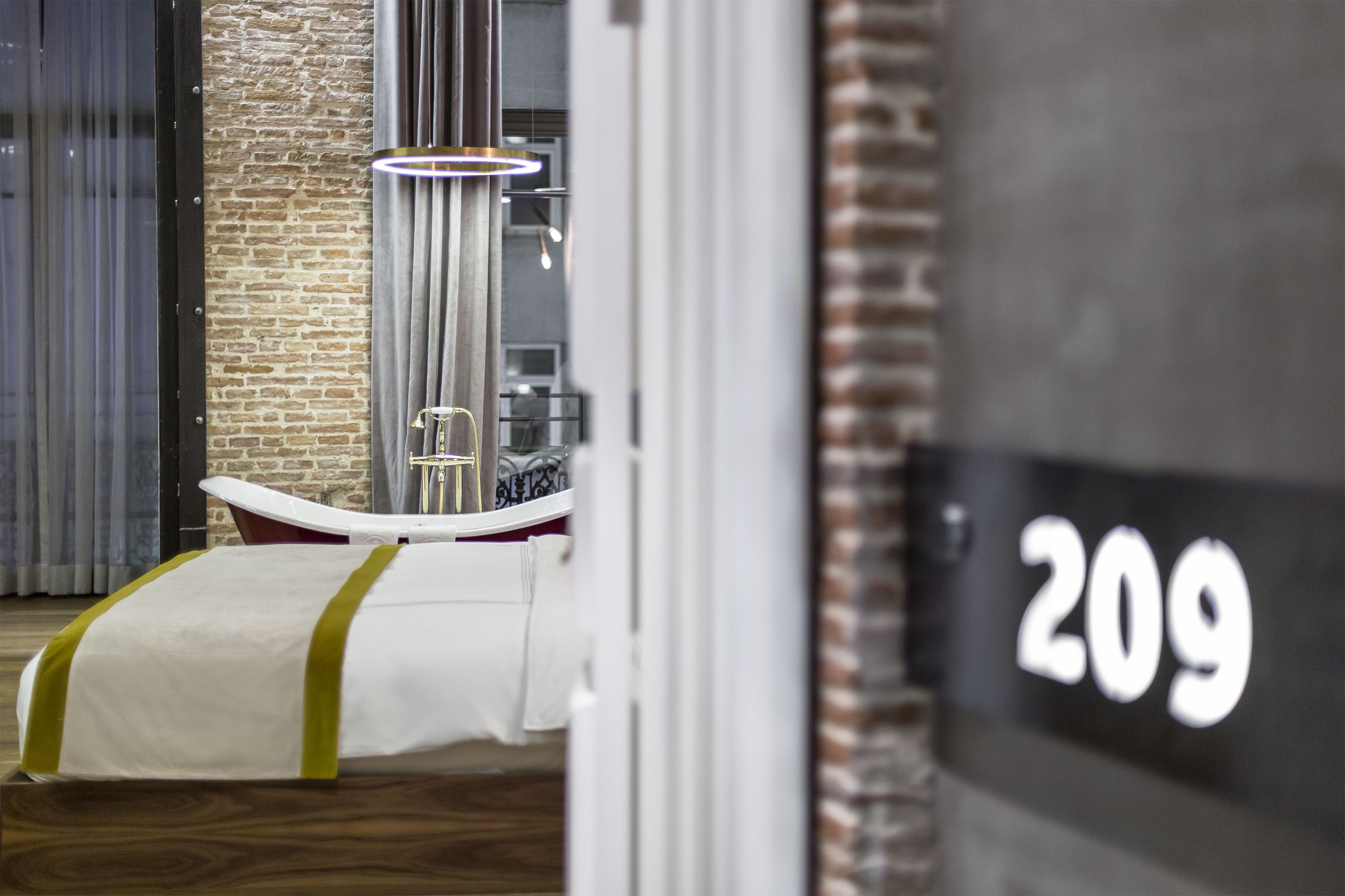 Ein Hotelzimmer mit der Nummer 209, einer Badewanne, Holzdielen und einer Ziegelwand.