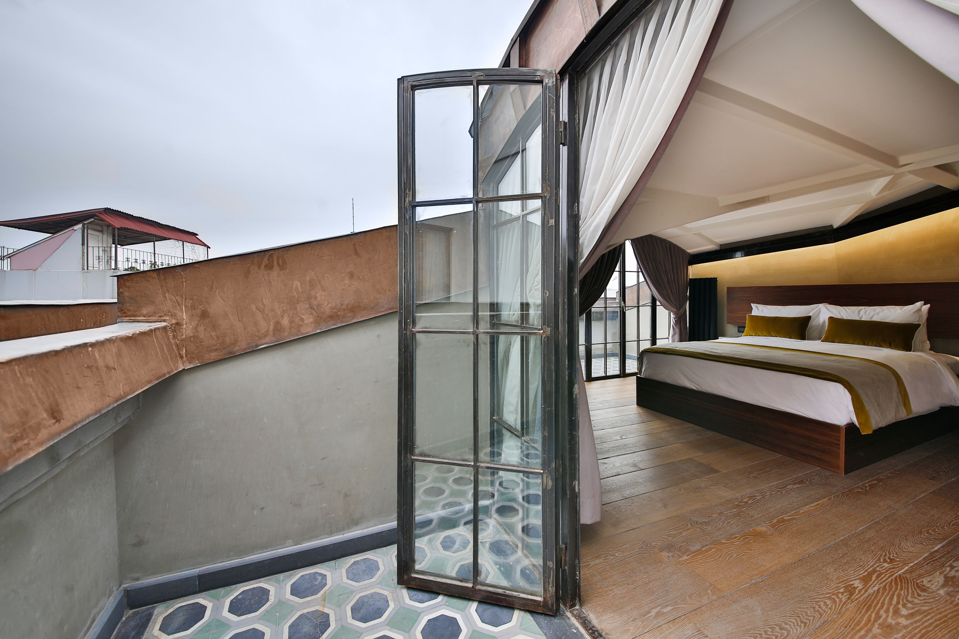 A modern hotel room with a large bed, a glass door leading to a balcony, and a view of the cityscape.