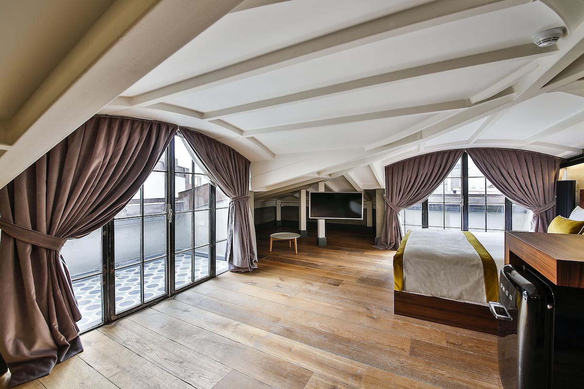 Habitación de hotel moderna con una cama grande, un escritorio y vistas de la ciudad a través de ventanales de techo a piso.