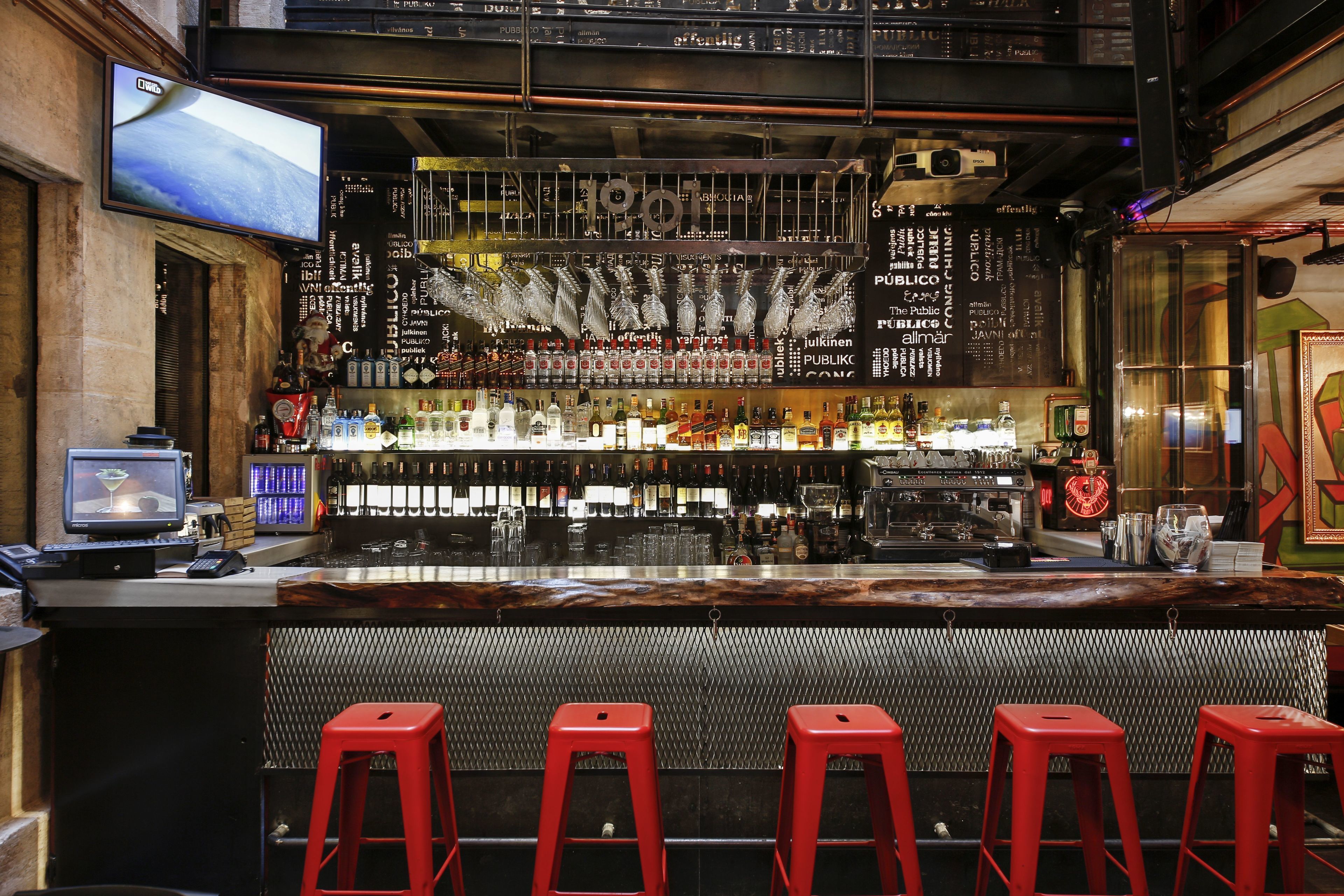 A bar with a wooden counter, red stools, and a TV screen.