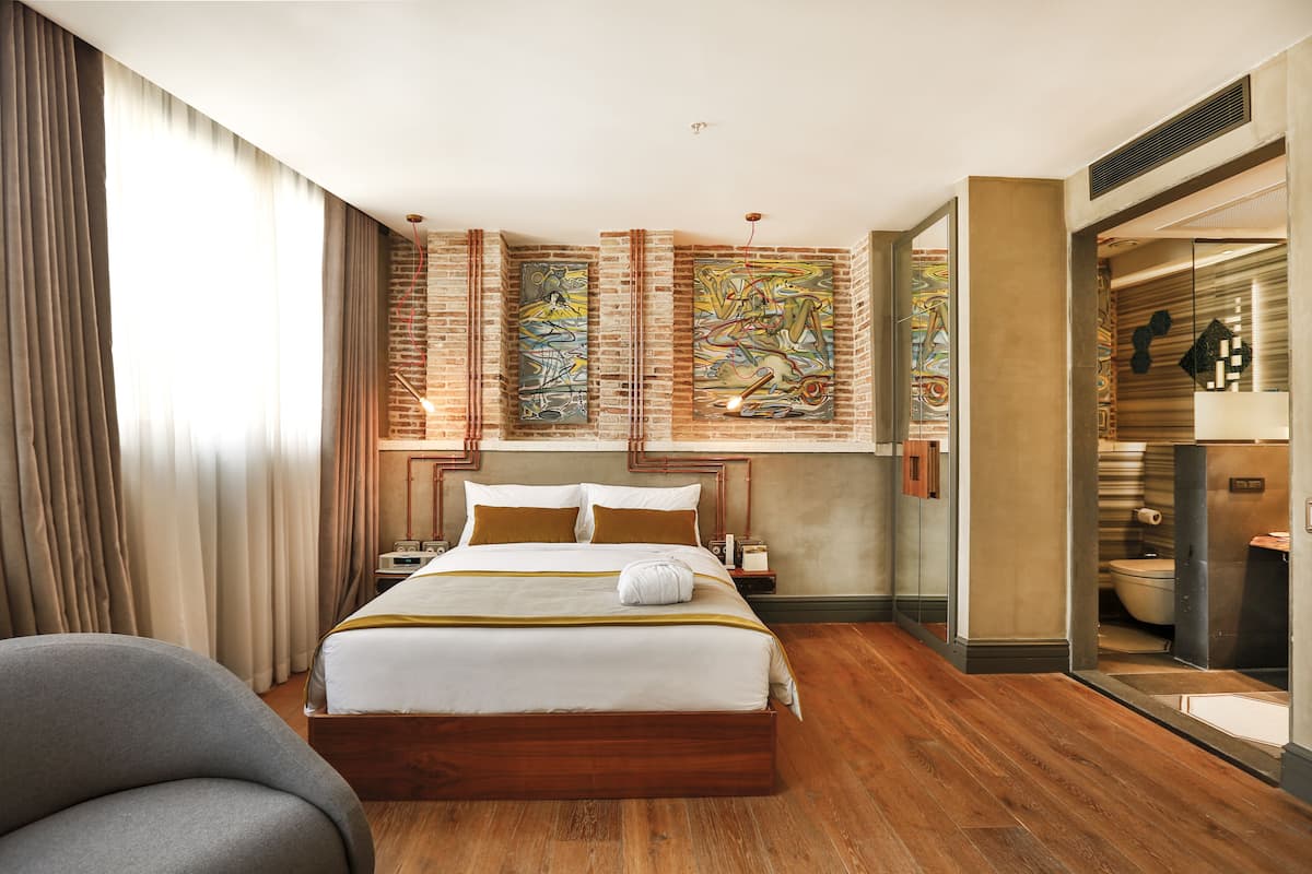 Habitación de hotel con una cama grande, piso de madera, baño moderno y obras de arte en las paredes.