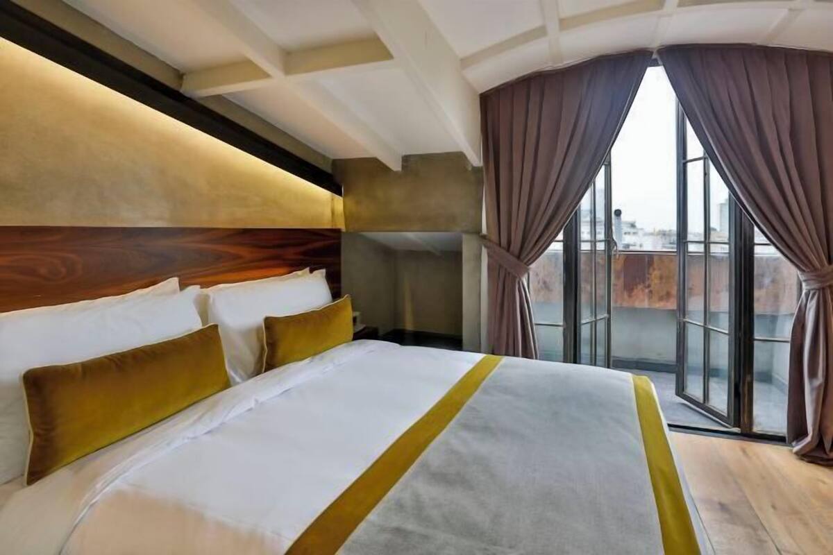 Una habitación de hotel con una cama grande, un cabecero de madera y vistas a través de un ventanal.