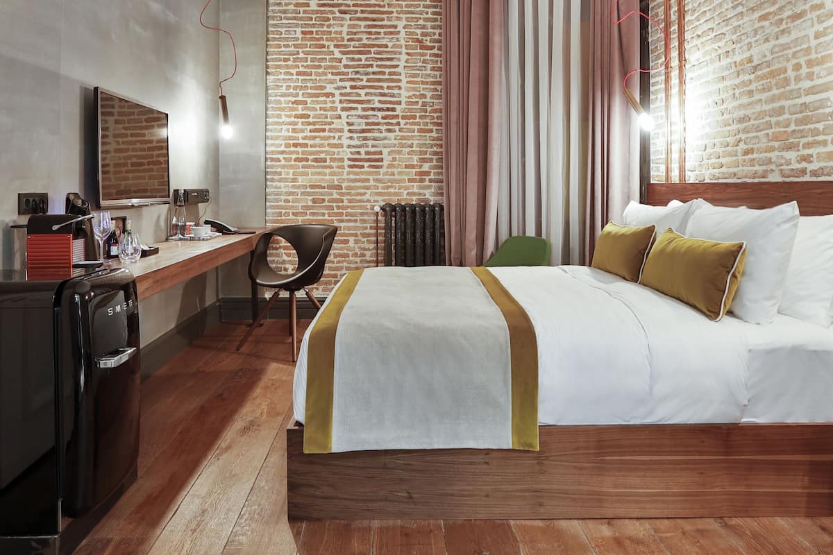 Habitación de hotel con pared de ladrillo, un escritorio de madera, una cama con ropa de cama blanca y una silla verde.