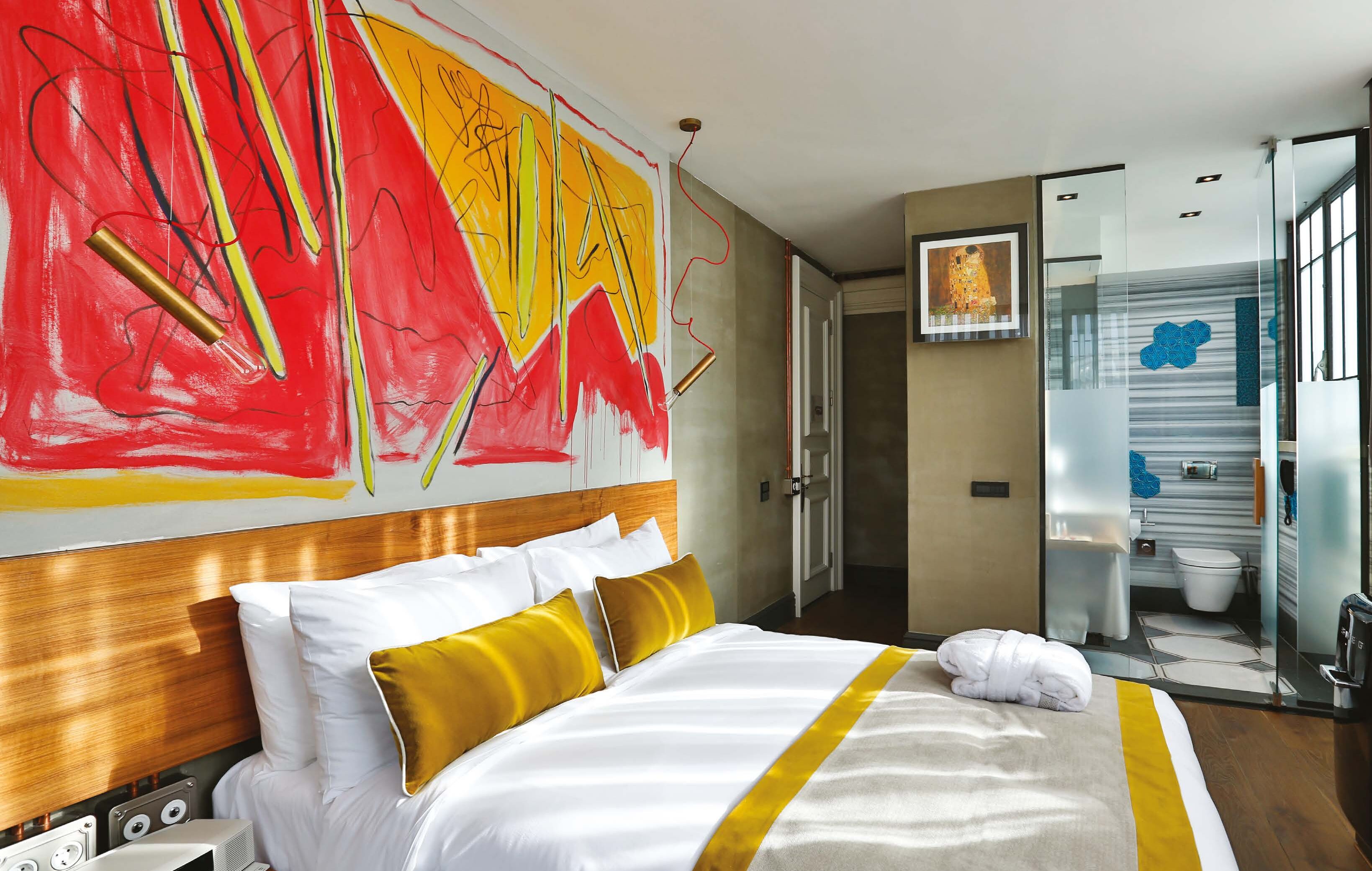 A hotel room with a large bed, a wooden headboard, and a vibrant abstract painting on the wall.