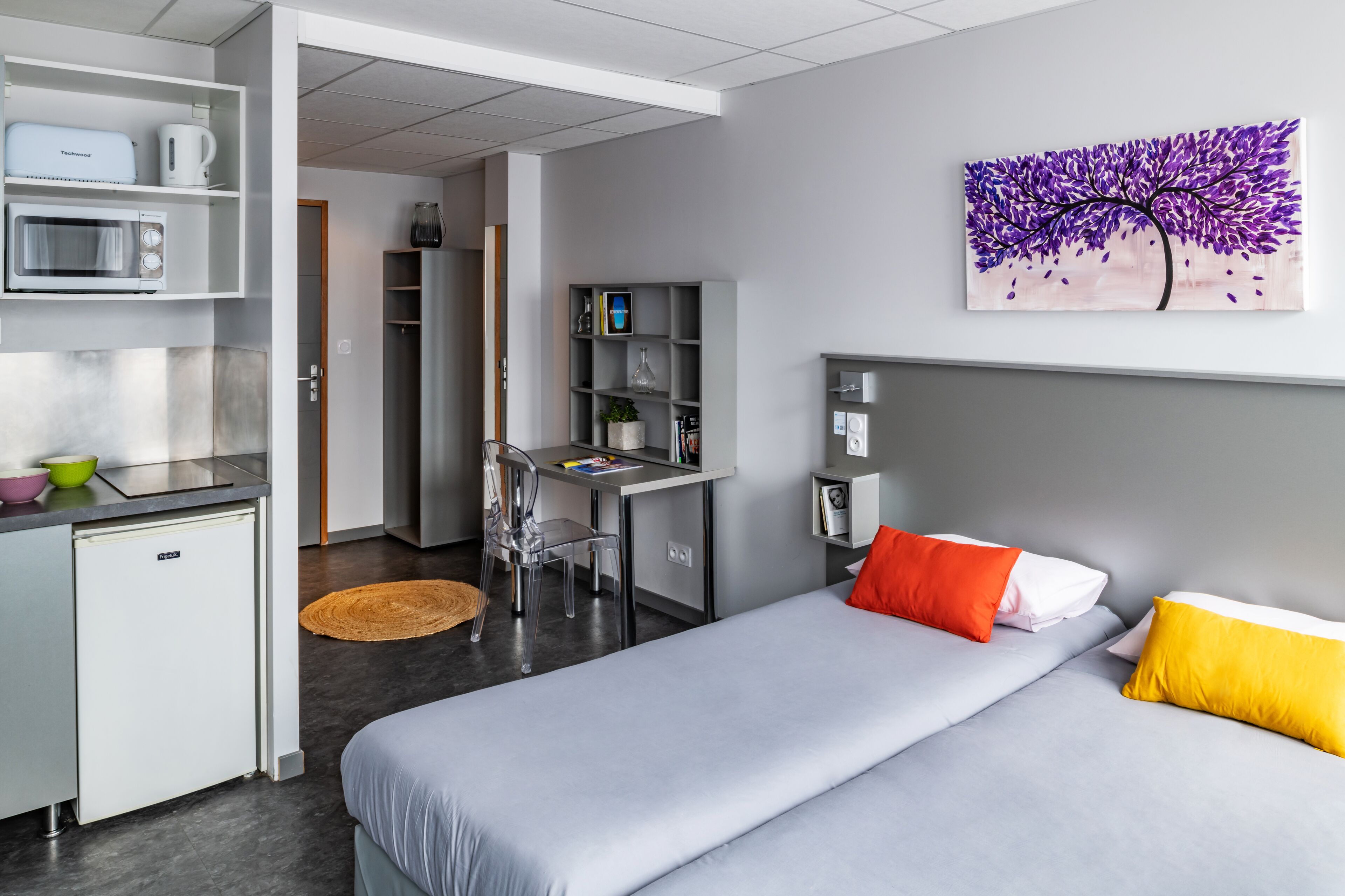 Une chambre d’hôtel moderne équipée d’un lit, d’un bureau, d’un four à micro-ondes et d’une bibliothèque.
