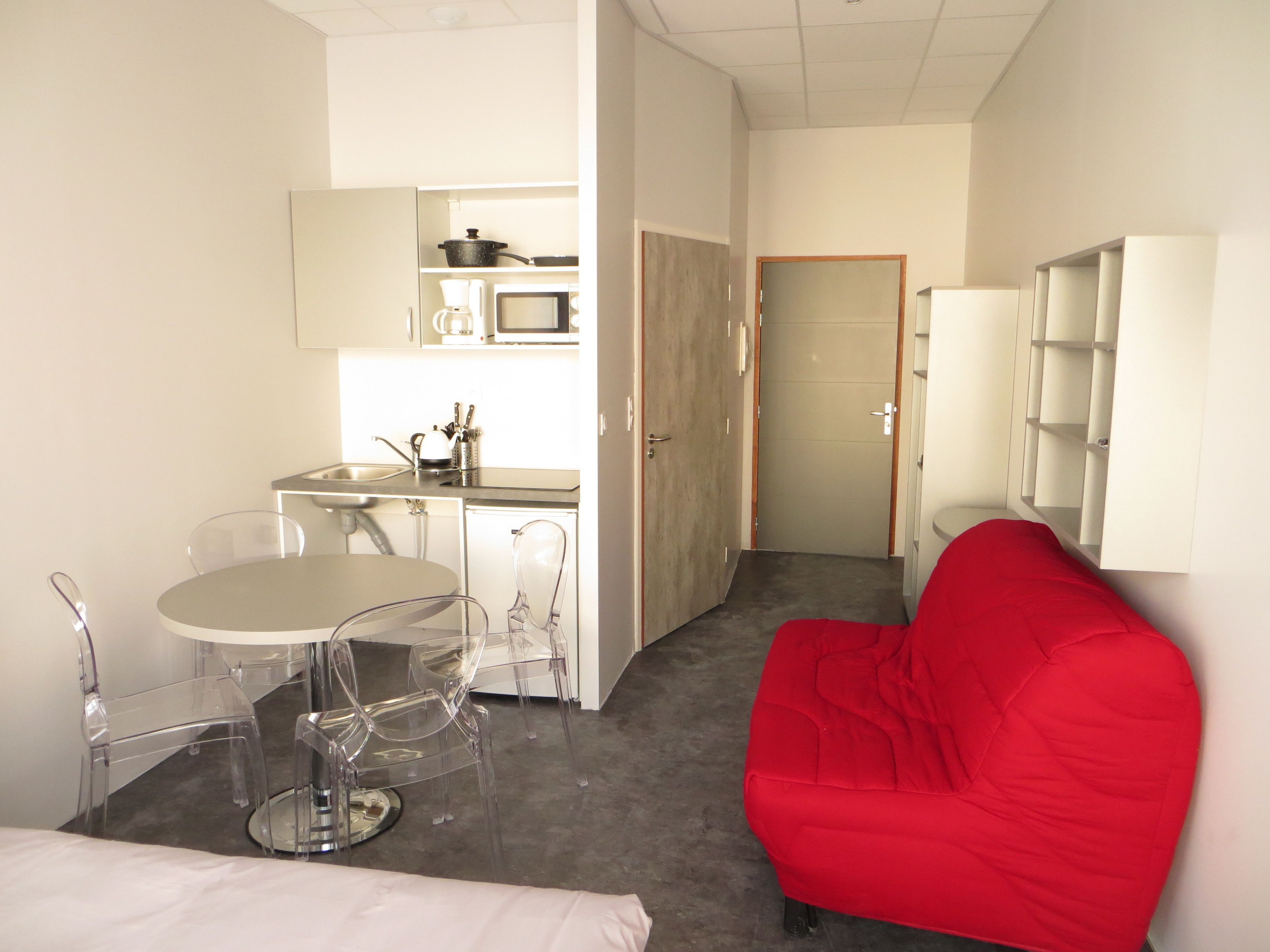 Un espacio habitable compacto con kitchenette, una zona de comedor con mesa y sillas, y un sofá rojo.
