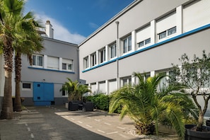 A modern building with a blue and white facade, a parking area with potted plants, and a clear sky.