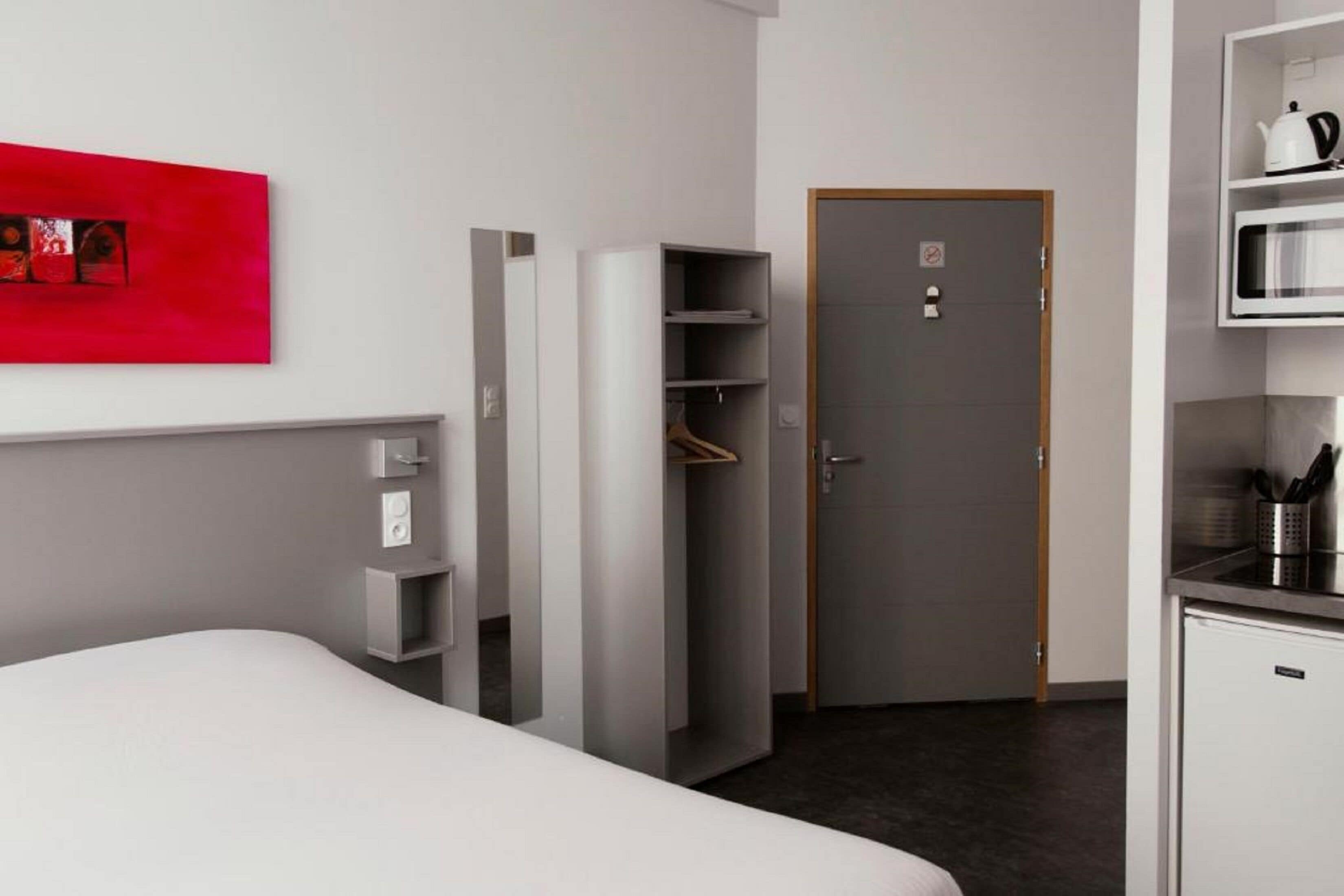 Een moderne hotelkamer met een bed, een garderobe, een deur en een kitchenette.