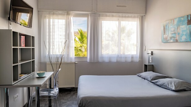 Een slaapkamer met een bed, een bureau met stoel, een boekenkast en een raam met gordijnen.