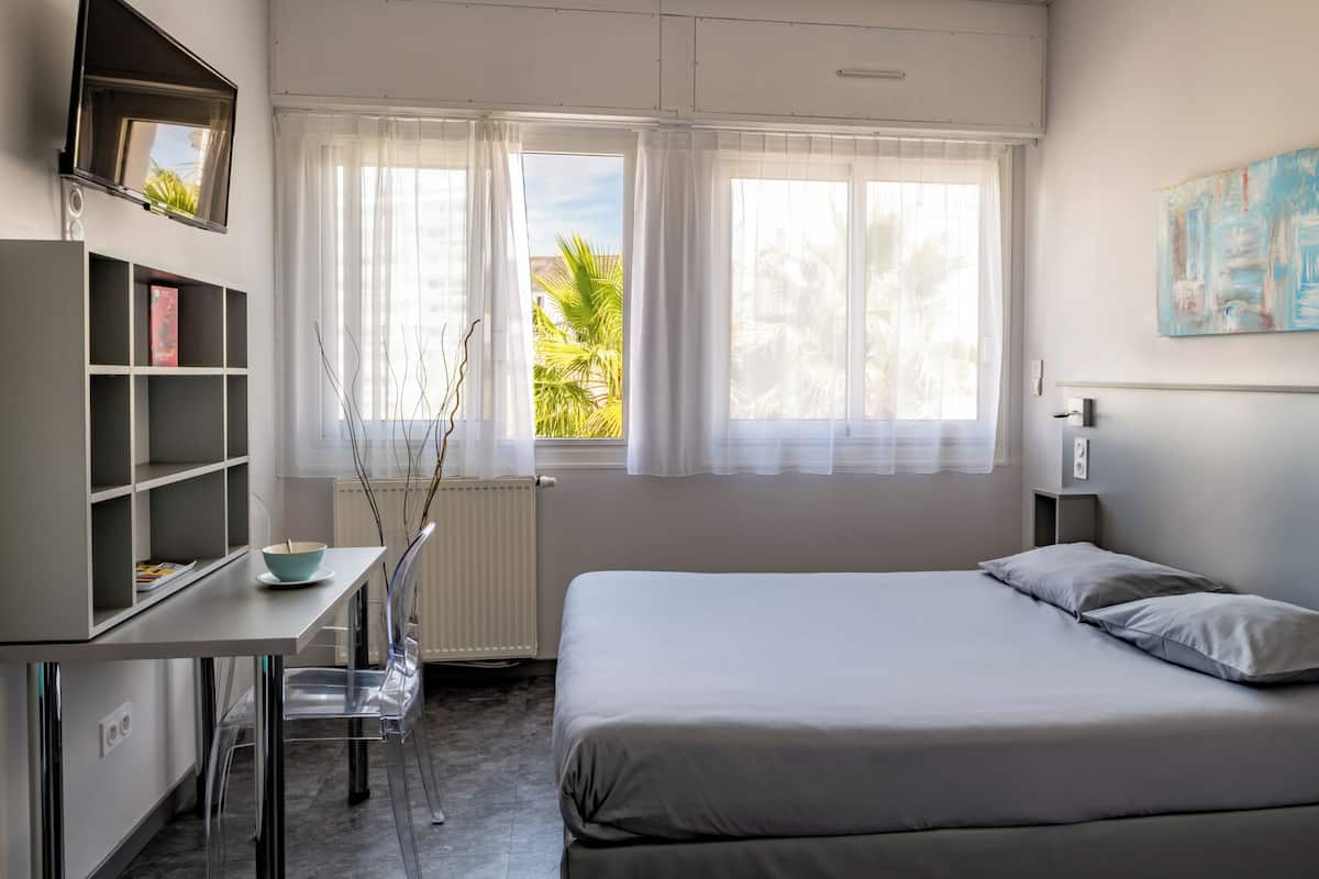 Een slaapkamer met een bed, een bureau met stoel, een boekenkast en een raam met gordijnen.