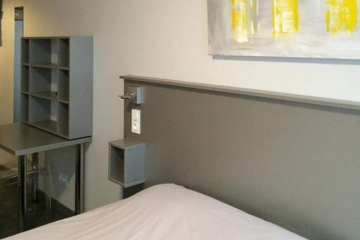 Een hotelkamer met een bed, een bureau, een stoel, een wandplank en een kunstwerk aan de muur.