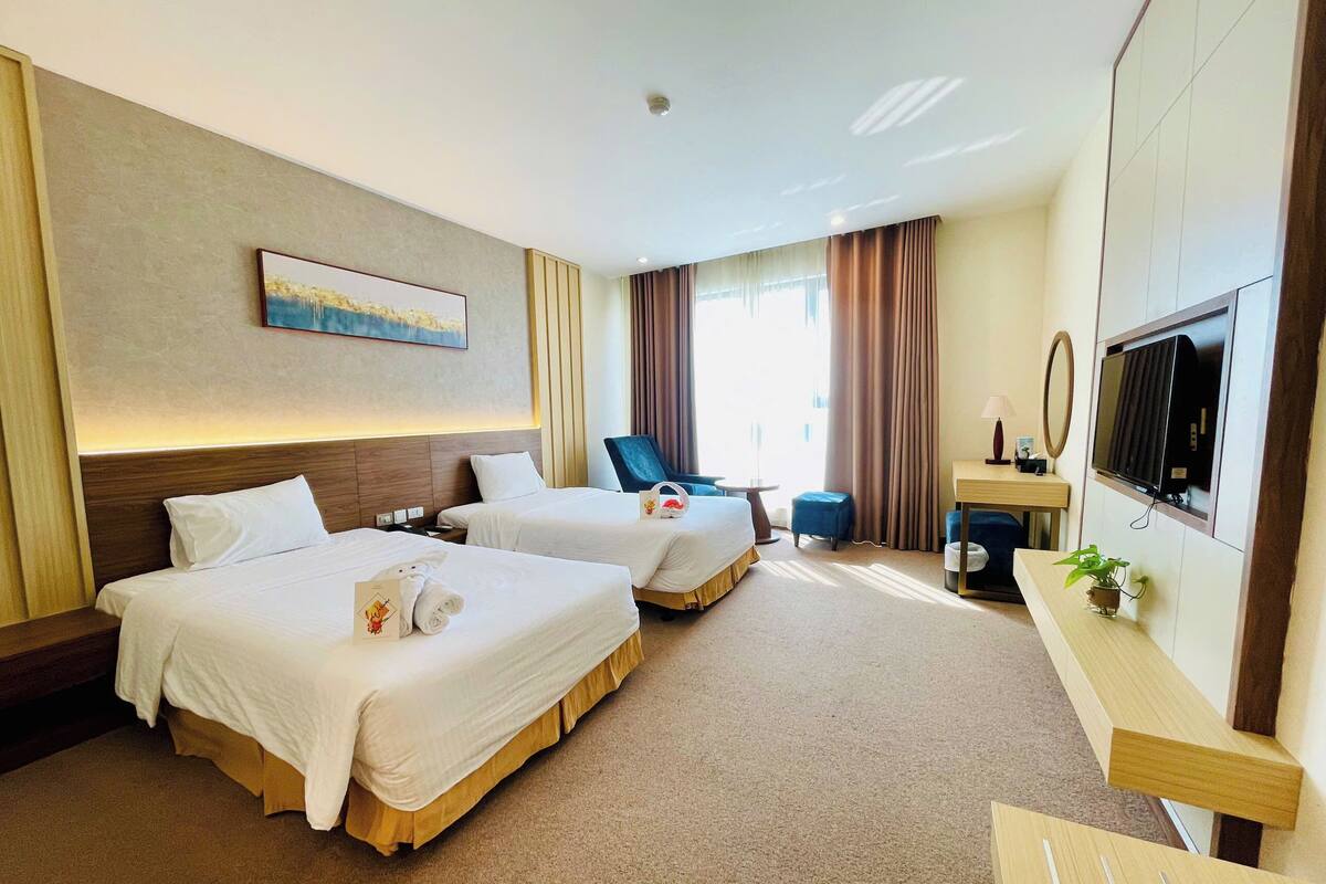 A hotel room with two beds, a desk, a chair, a TV, and a window with curtains.