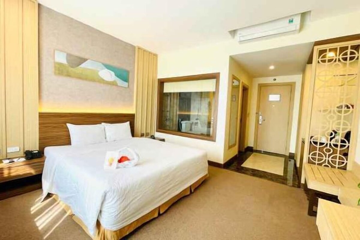 A hotel room with a large bed, a window, and a door leading to a bathroom.