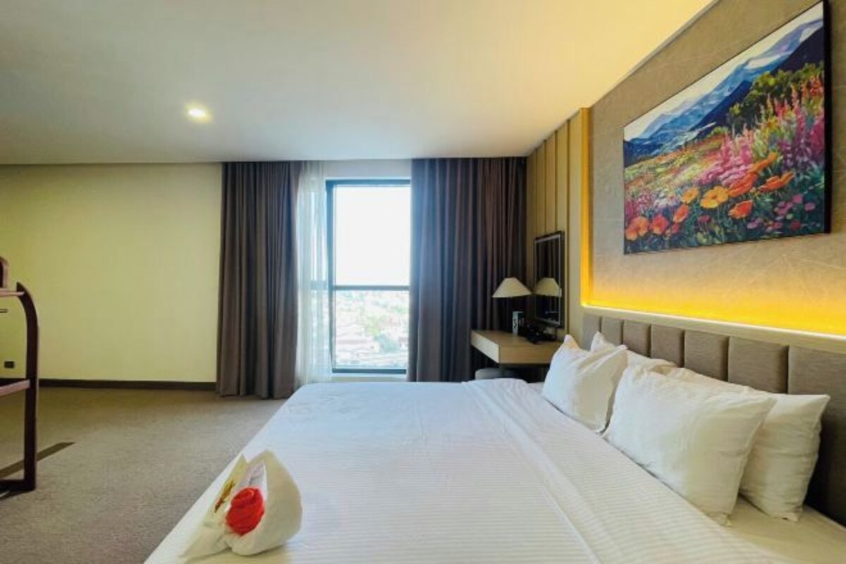 Een hotelkamer met een groot bed, een bureau en een schilderij aan de muur.