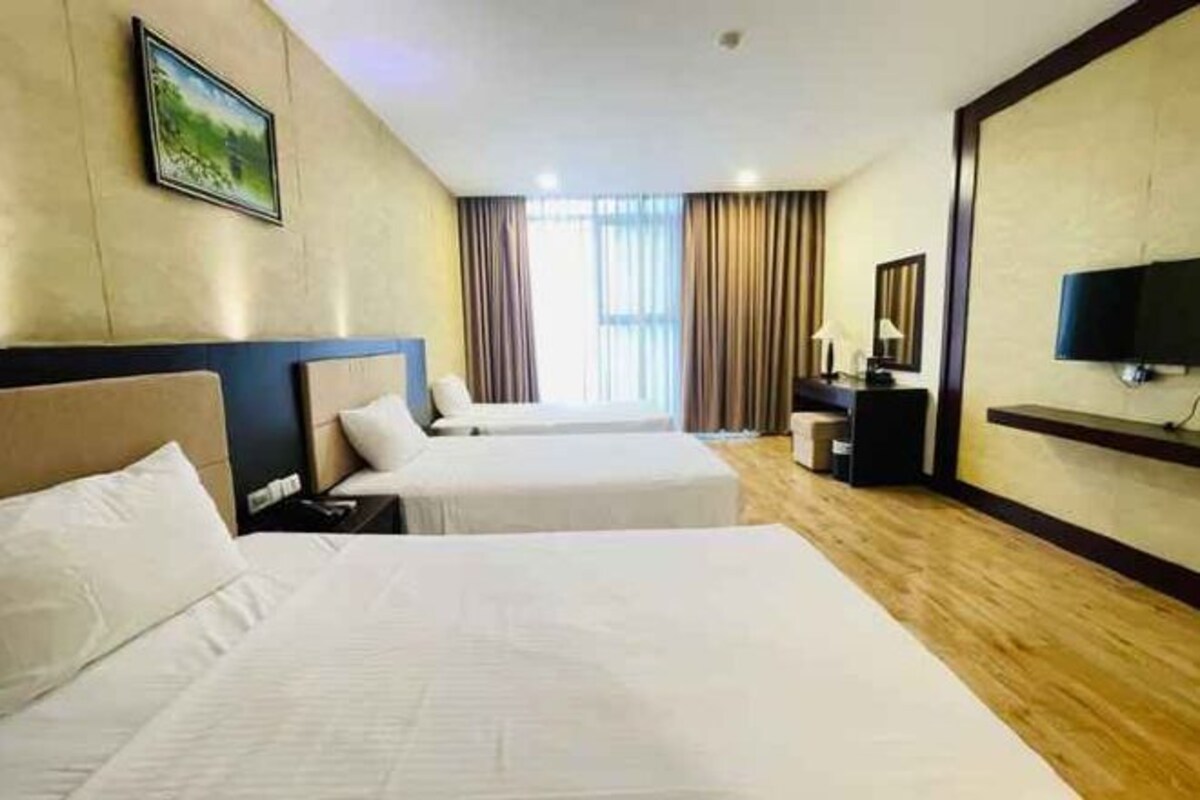 Een hotelkamer met twee bedden, een flatscreen televisie, een bureau met lamp en een raam met gordijnen.