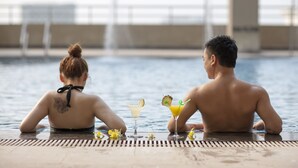 Deux personnes sont assises au bord d’une piscine, avec des boissons et des fleurs à proximité.