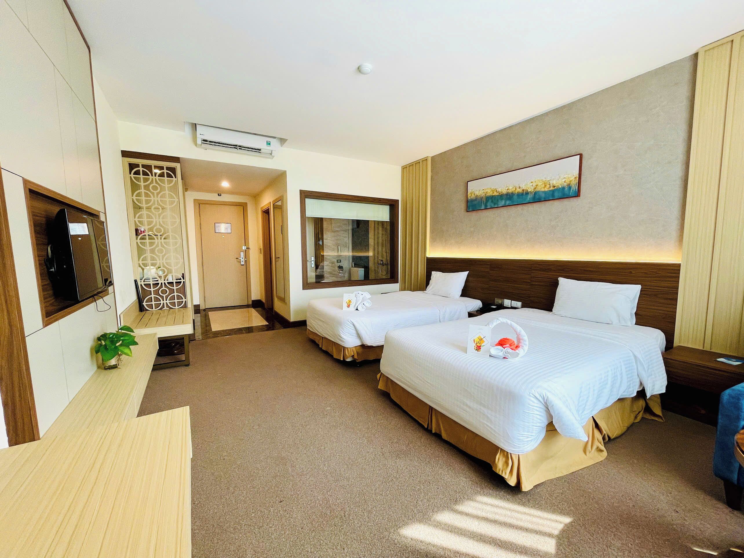 A hotel room with two beds, a TV, a painting, and a small plant.