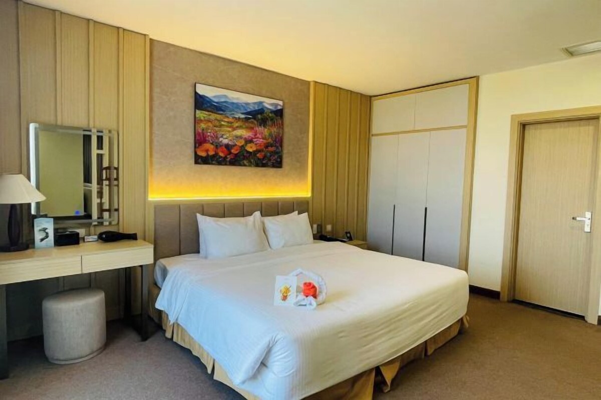 Quarto de hotel com cama, mesa de cabeceira, abajur e um quadro na parede.