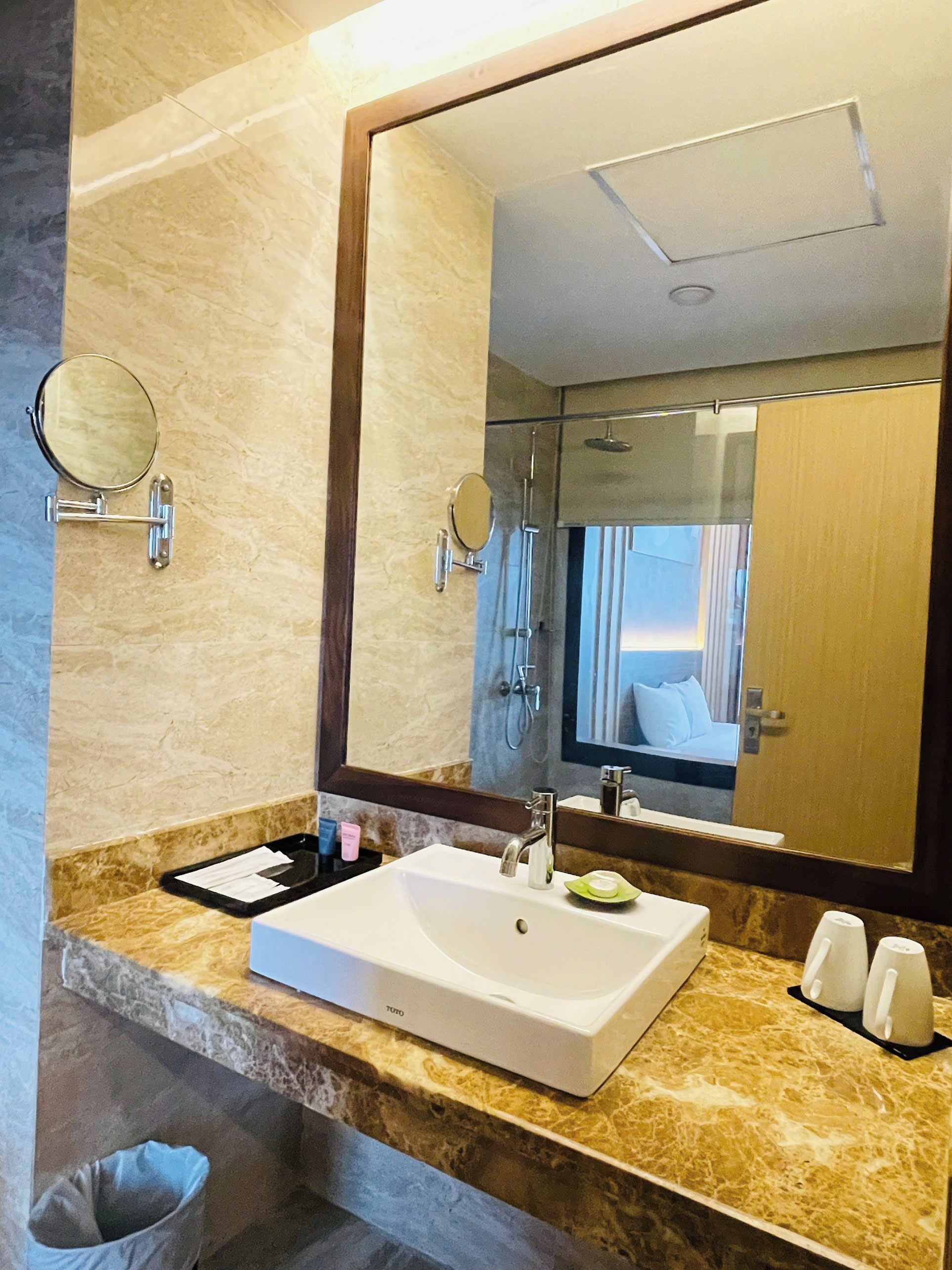 A bathroom with a large mirror, a white sink, and a shower.