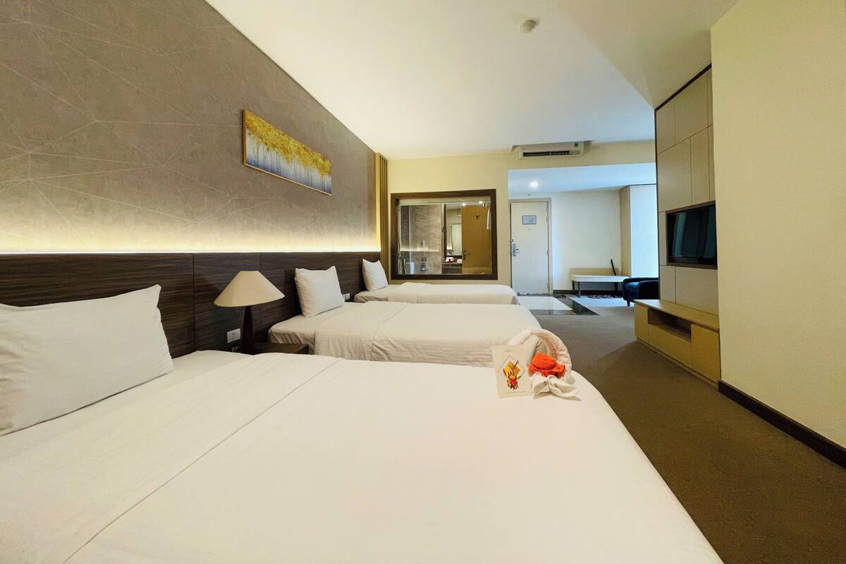 A hotel room with two beds, a TV, a desk, and a bathroom visible through an open door.