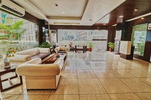 Un hall de hotel con zona de estar, mostrador de recepción y vistas a la ciudad a través de amplios ventanales.