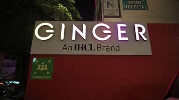 Señal de 'GINGER An IHCL Brand' con un símbolo de punto de encuentro y, al fondo, un letrero del Hospital de Columna Narayan.