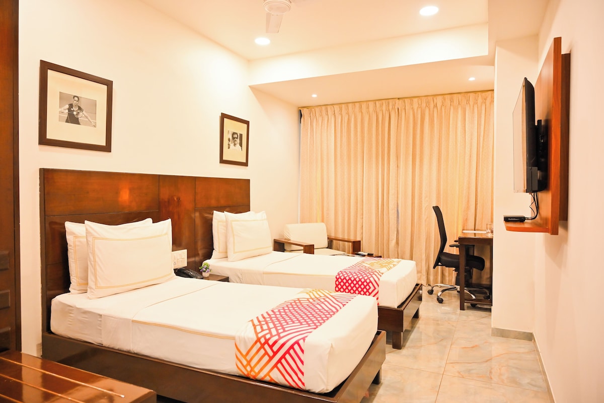 A hotel room with two beds, a desk, a chair, a television, and a window with curtains.