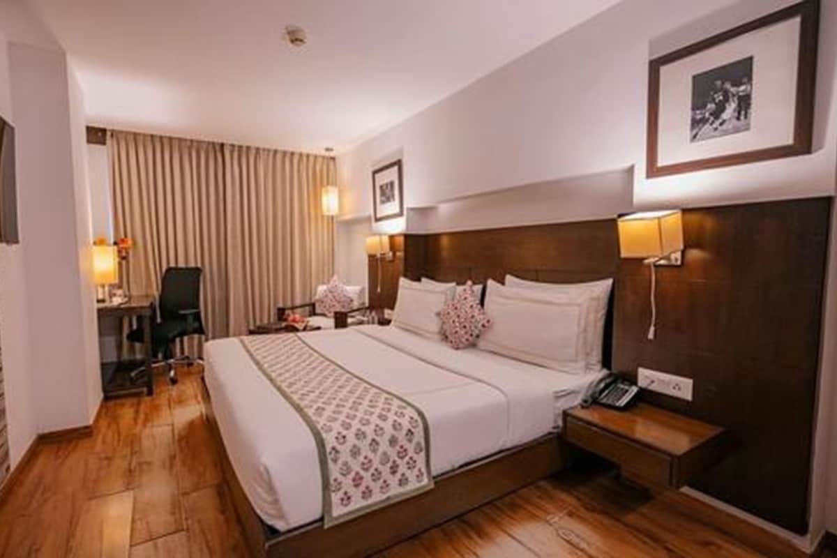 A hotel room with a large bed, a desk, a chair, a bedside table, a lamp, and a framed picture on the wall.