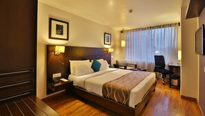 A hotel room with a large bed, bedside tables, a desk, and a chair. - Ginger Vadodara,Alkapuri (Vadodara)