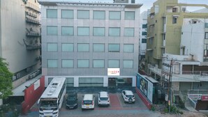 A multi-story building with a central entrance, parking lot, and adjacent smaller structures. - Ginger Vadodara,Alkapuri (Vadodara)