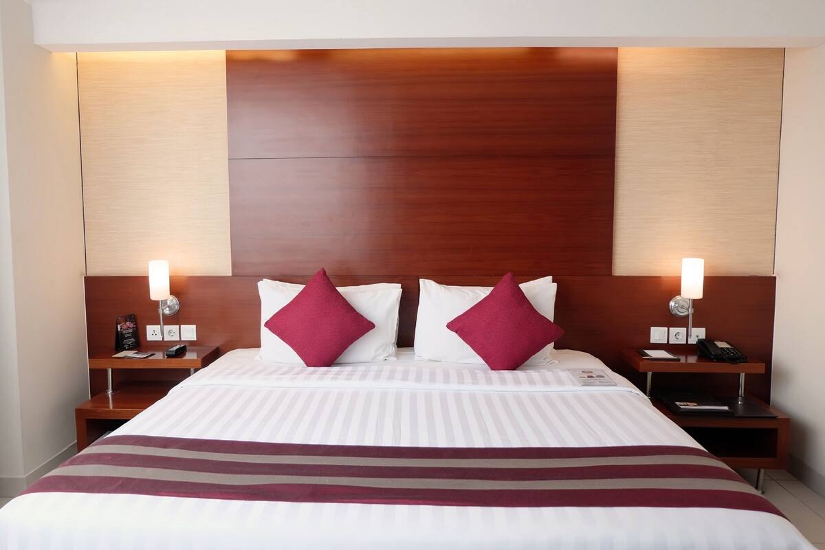 A hotel room with a large bed, two nightstands, a wooden headboard, and a striped bedspread.