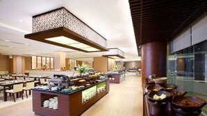 Un moderno hall de hotel con área de buffet, arreglos de asientos y un ventanal con vistas.