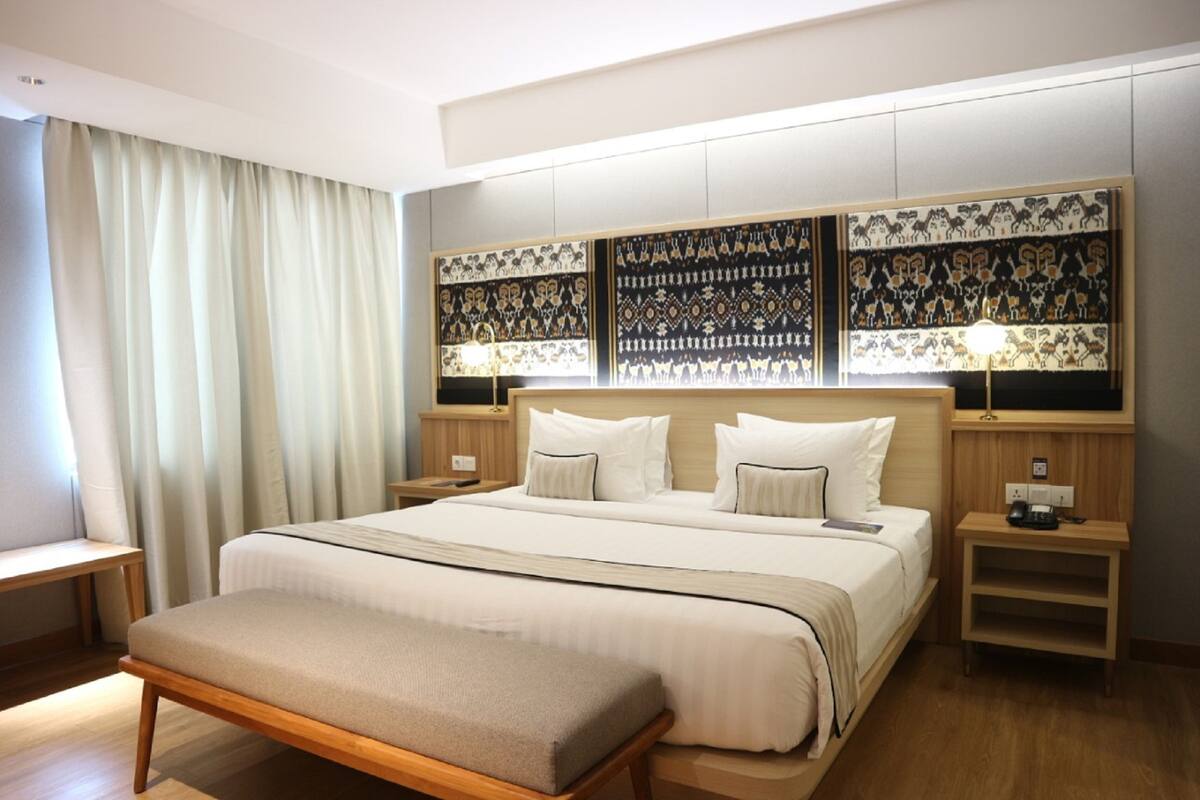 A modern hotel room with a large bed, bedside tables, a bench, and decorative wall panels.