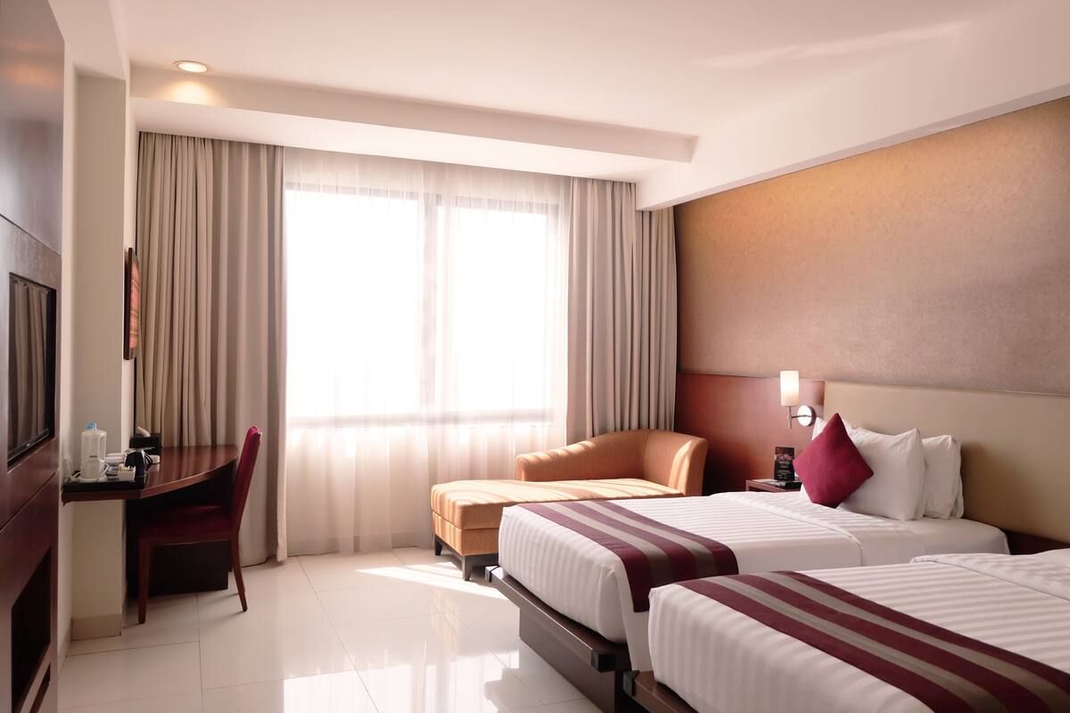 A hotel room with two beds, a desk, and a chair.