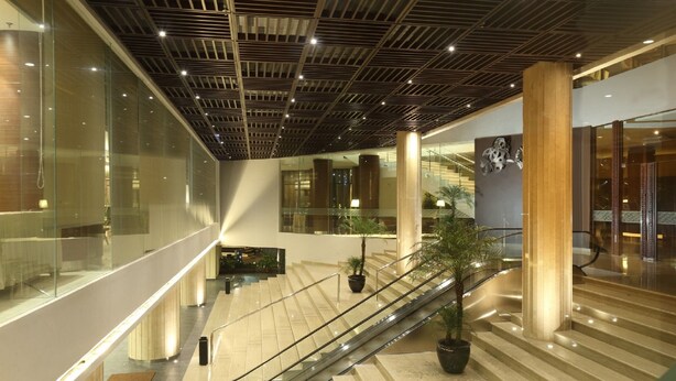 Un interior moderno con una escalera mecánica, paredes de vidrio y un techo con diseño de cuadrícula.