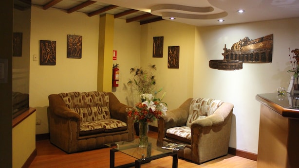 Una sala de estar con dos sofás, una mesa de centro y un jarrón con flores. Se observan obras de arte en la pared y un aparador de madera.