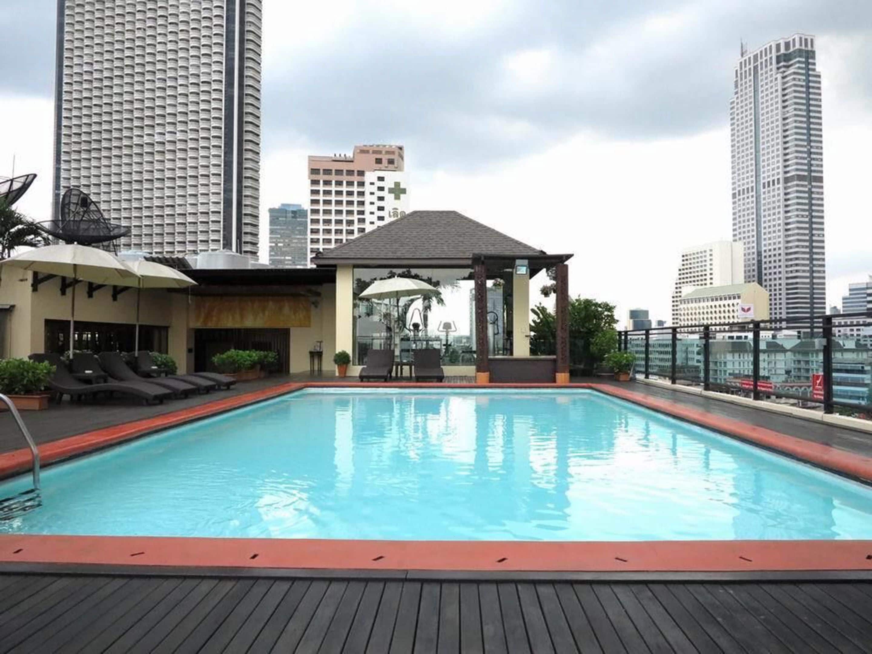 A rooftop pool with lounge chairs and a gazebo, surrounded by high-rise buildings.