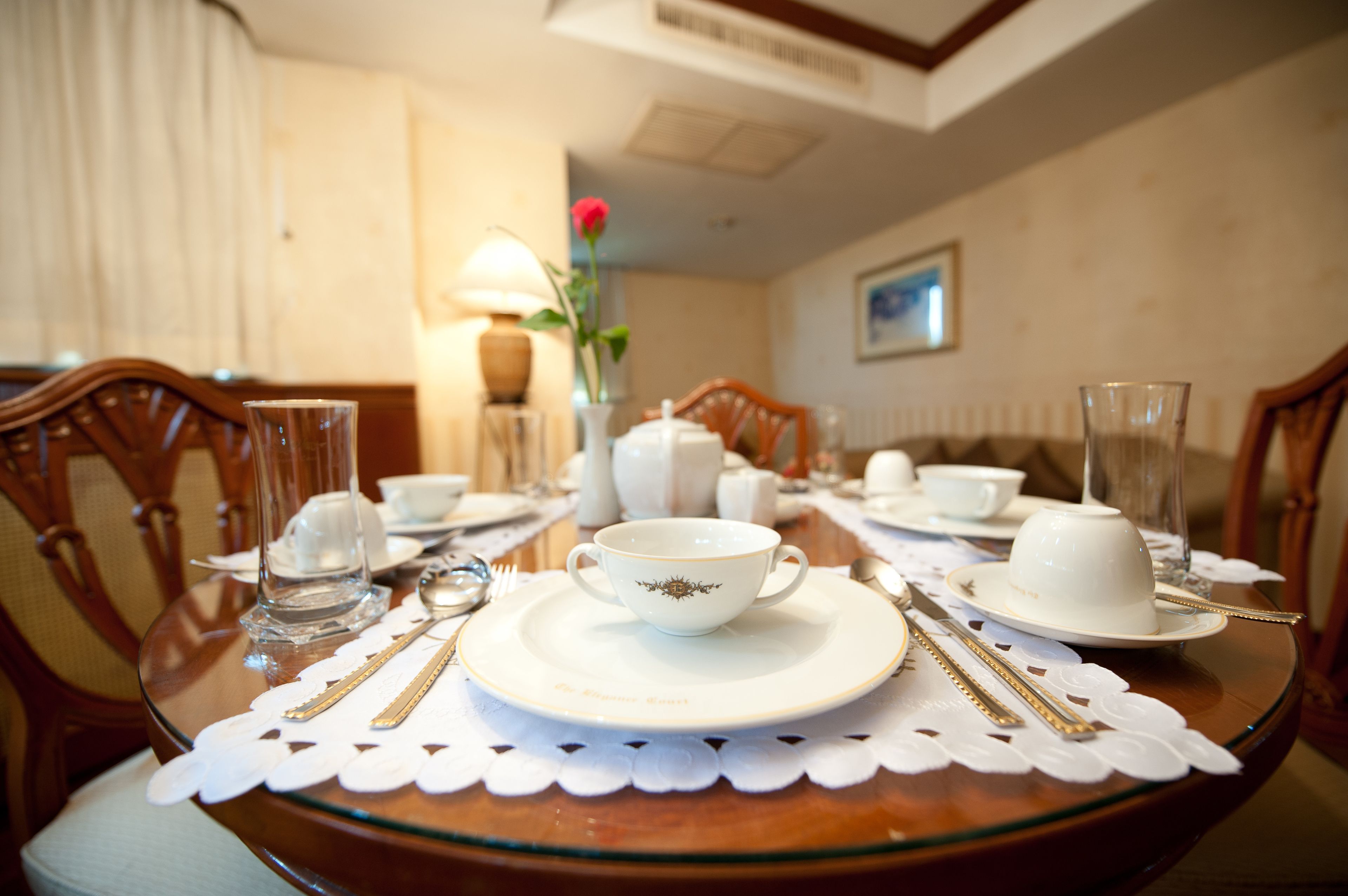 A dining table set with white plates, cups, and cutlery, surrounded by wooden chairs.