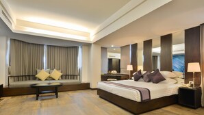 A modern hotel room with a large bed, a sofa, a coffee table, and a desk with a lamp. - The Grand Sathorn (Bangkok)