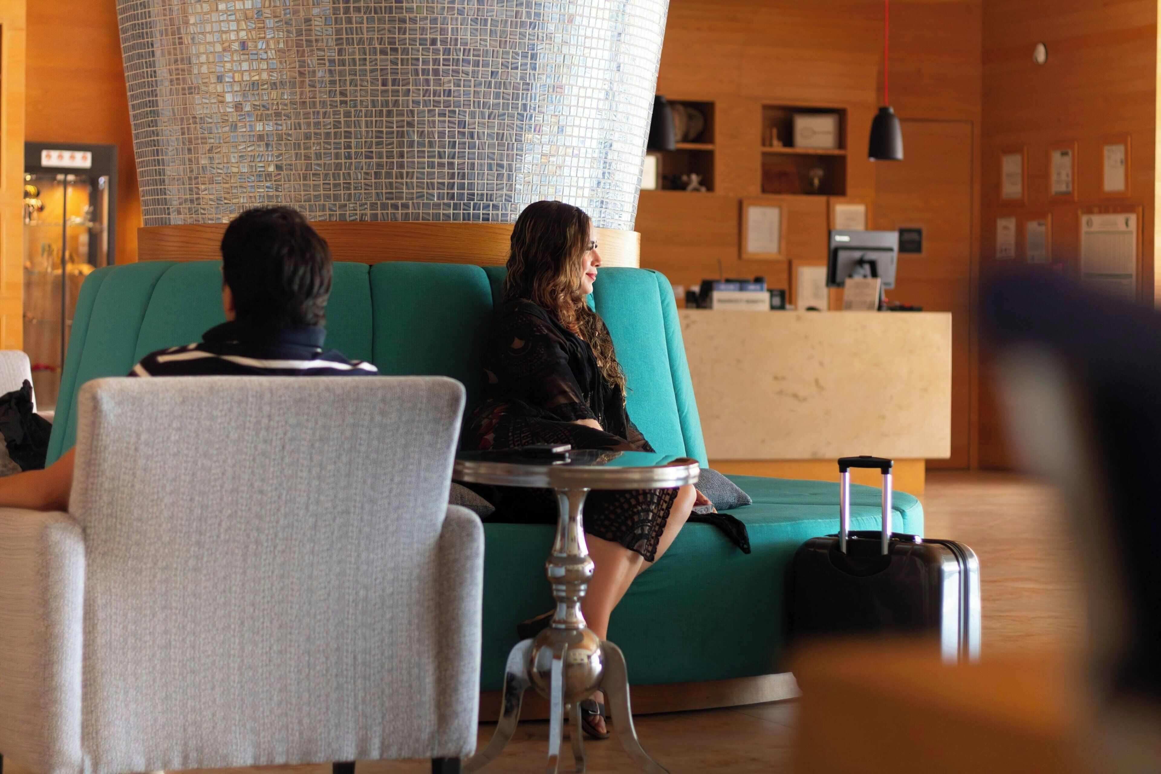 A lobby with a teal sofa, a reception desk, and a table with a suitcase.