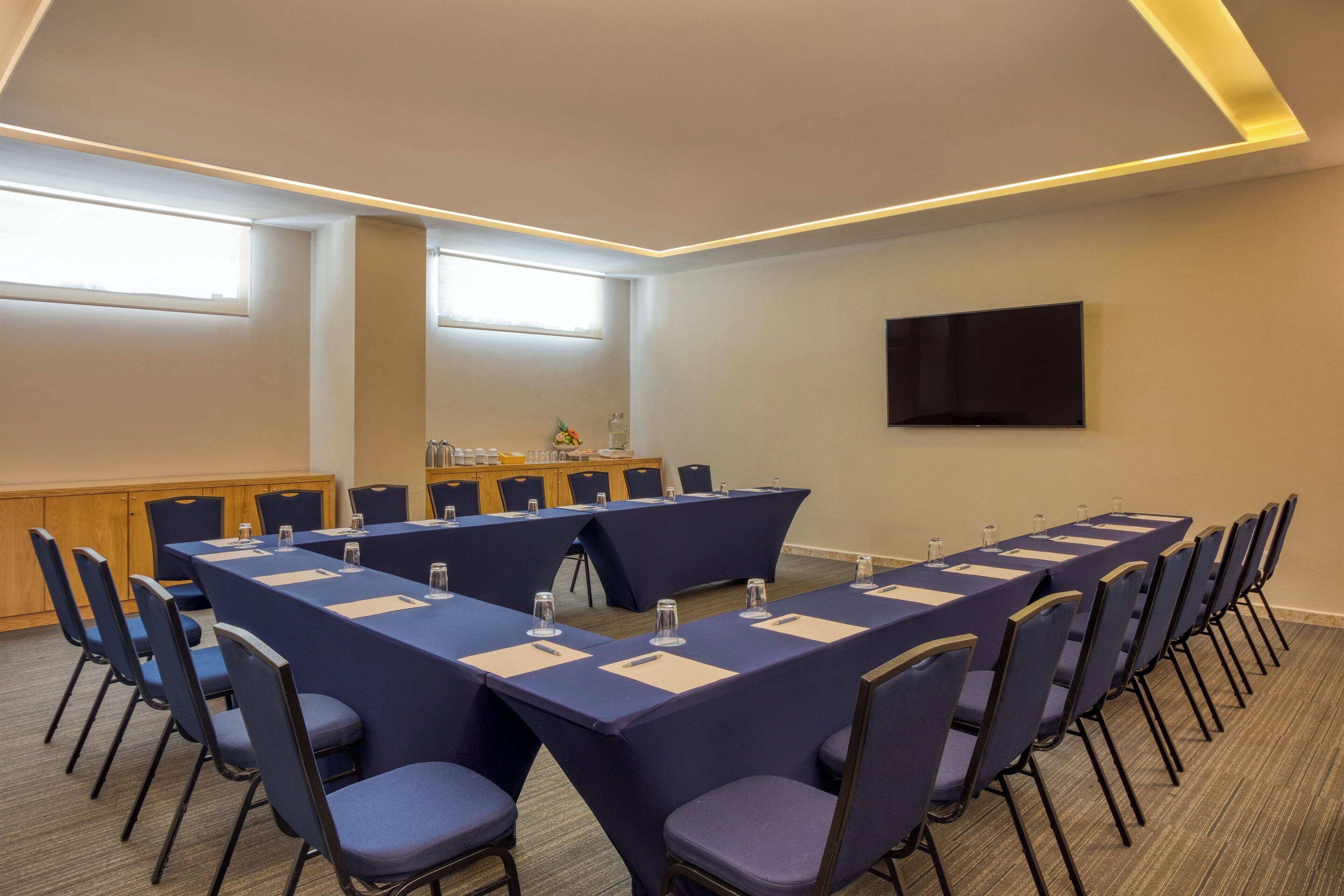 Ein Konferenzraum mit einem langen Tisch, Stühlen, einem Rednerpult und einem Flachbildfernseher an der Wand.