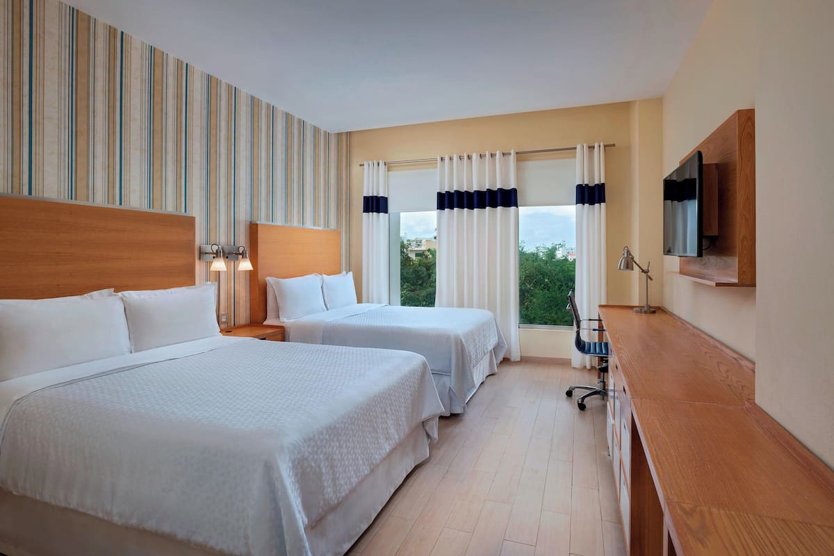 A hotel room with two beds, a wooden desk, a TV, and a window with curtains.