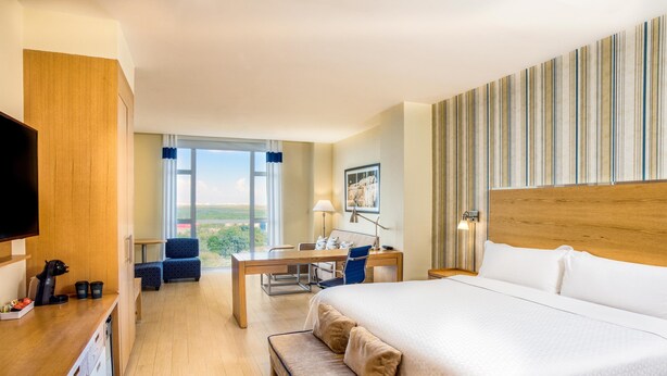 A hotel room with a large bed, a desk with a chair, a bench, a TV, and a window with a view. - Four Points by Sheraton Cancun Centro (Cancun)