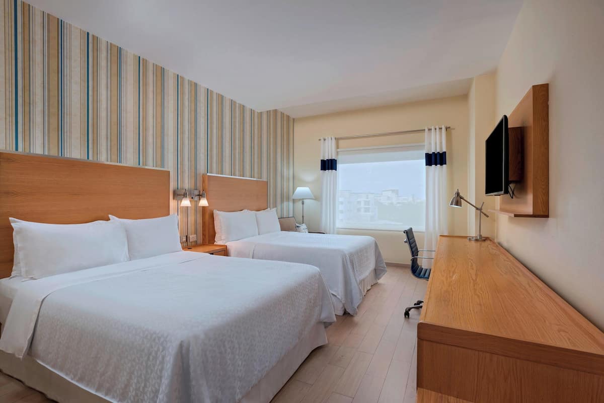 A hotel room with two beds, a wooden desk, a TV, and a window with curtains.