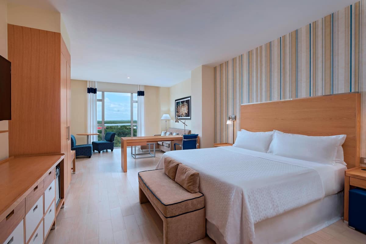 A hotel room with a large bed, a desk, a chair, and a view of the outdoors.