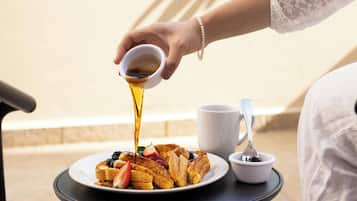 Een ontbijt met Frans toast, aardbeien, blauwe bessen, een kop koffie en een klein schaaltje siroop.