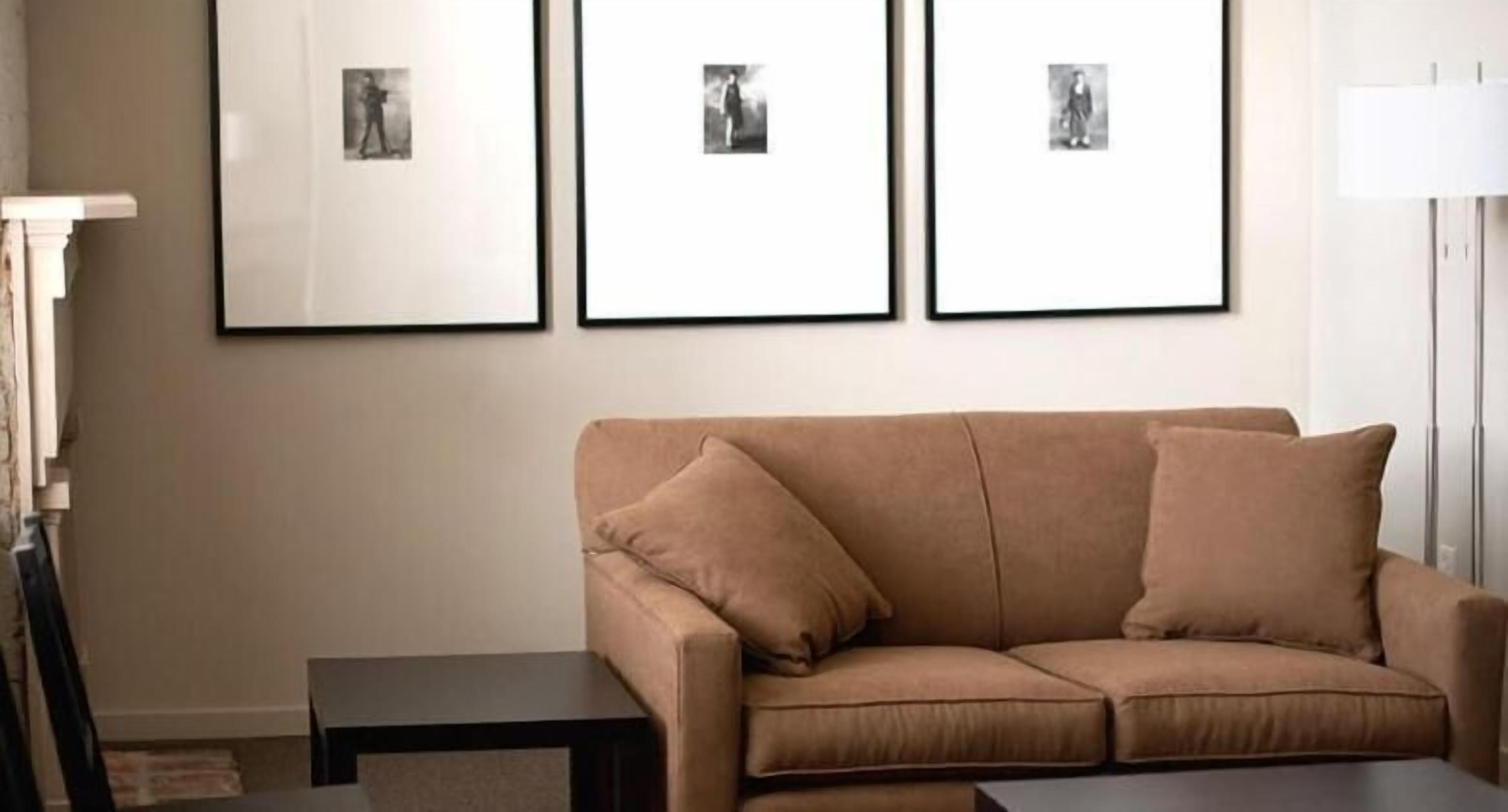 A living room with a beige sofa, a small table, and three framed pictures on the wall.